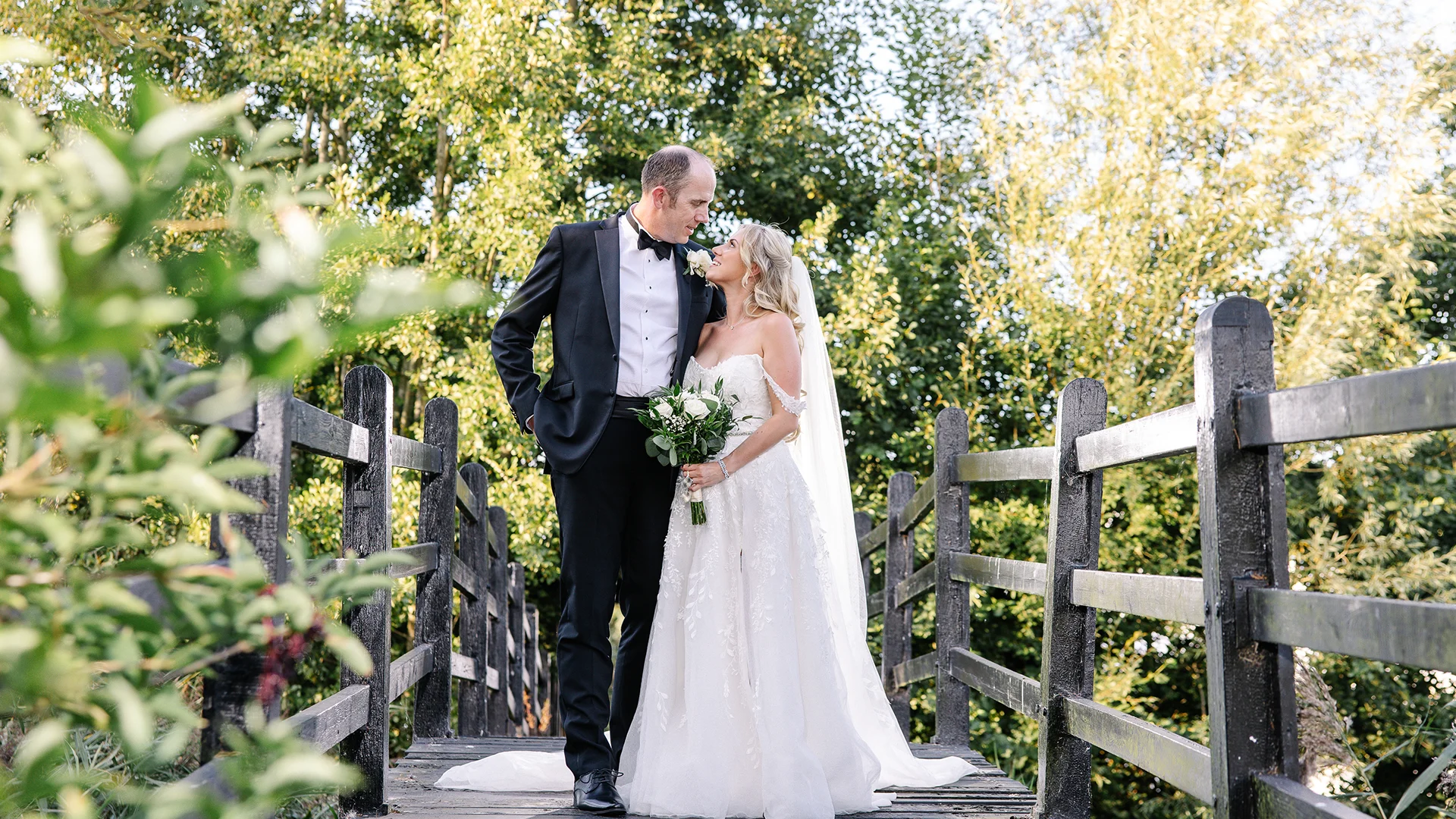 A newlywed couple sharing a romantic moment by the historic moated bridge, highlighting the breathtaking Wedding Photography Locations Essex available at Prested Hall.