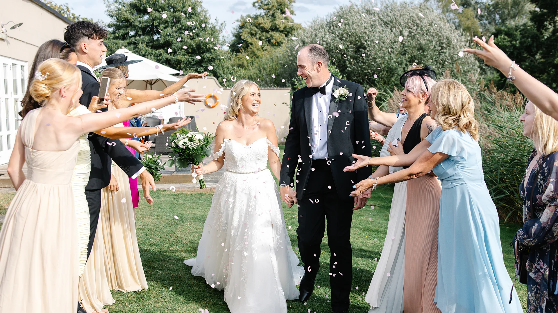 An elegant bridal party walking across a historic moated bridge, showcasing the breathtaking scenery of a premium UK destination wedding venue.